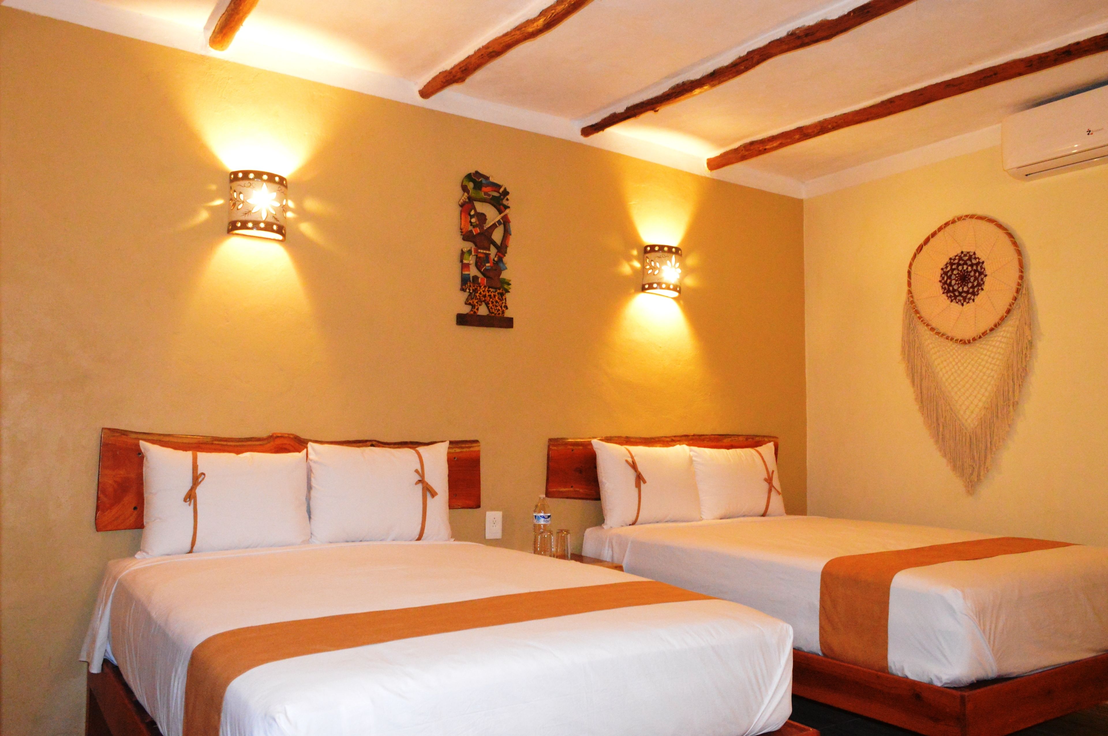 A hotel room with two beds, wooden headboards, wall-mounted lights, and a dreamcatcher decoration.