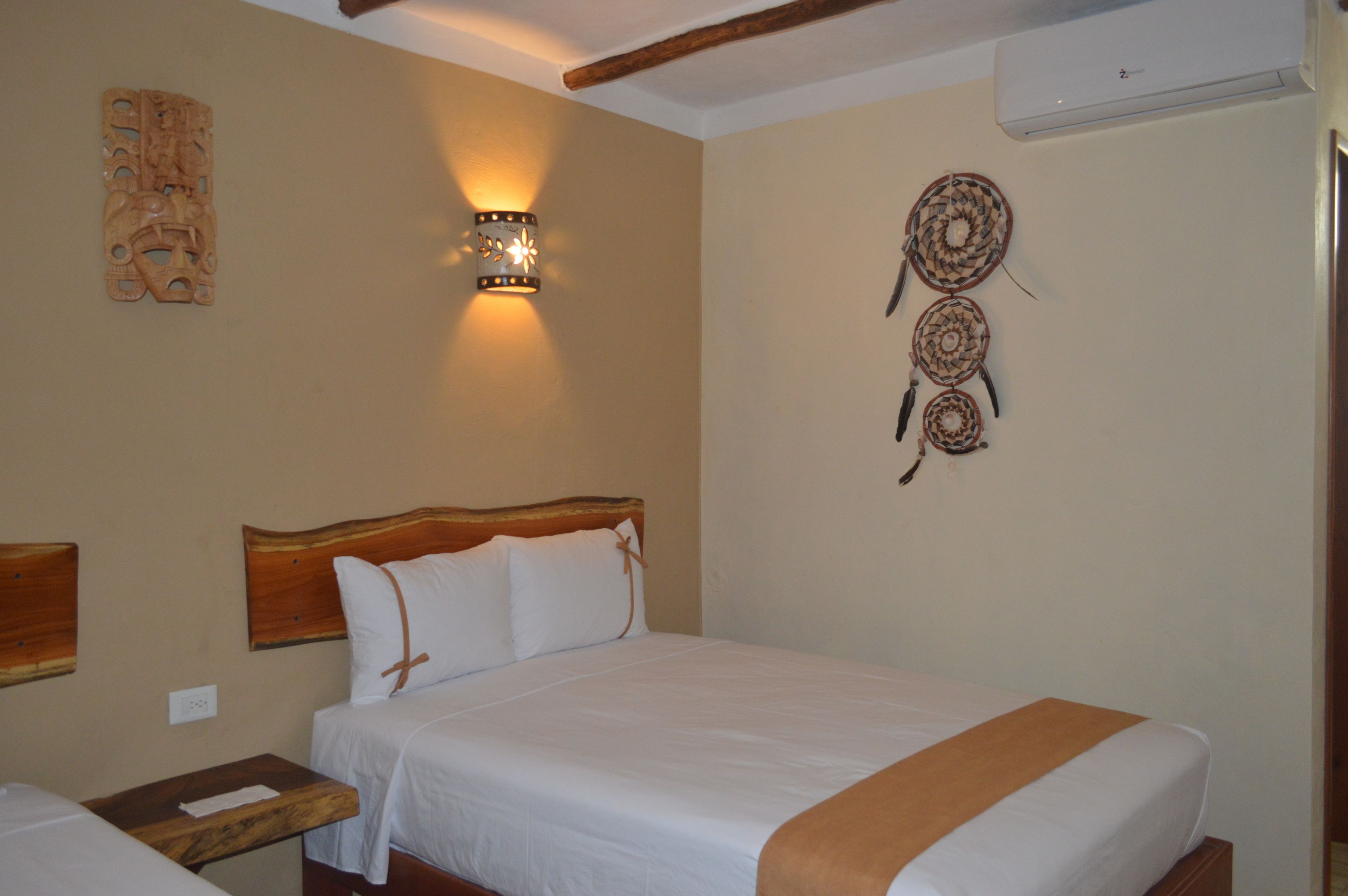 A hotel room with a wooden headboard, a bed with white bedding, a nightstand, a wall-mounted light fixture, and decorative wall art.