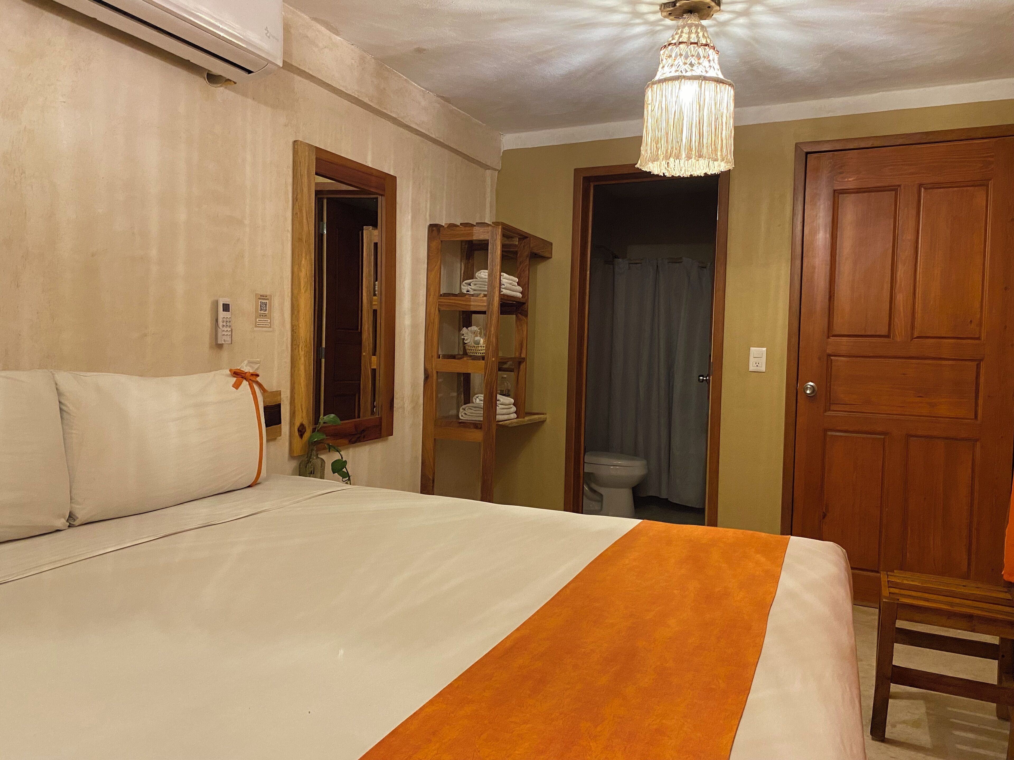 Habitación de hotel con cama, armario de madera, baño con inodoro y cortina de ducha, y un candelabro.