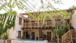 Un edificio de piedra de dos pisos con un balcón, una escalera y un pequeño área de piscina.
