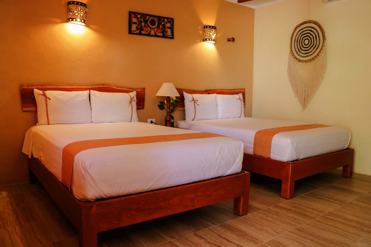 Two double beds with wooden frames and white bedding, a wall-mounted artwork, and a decorative wall hanging.