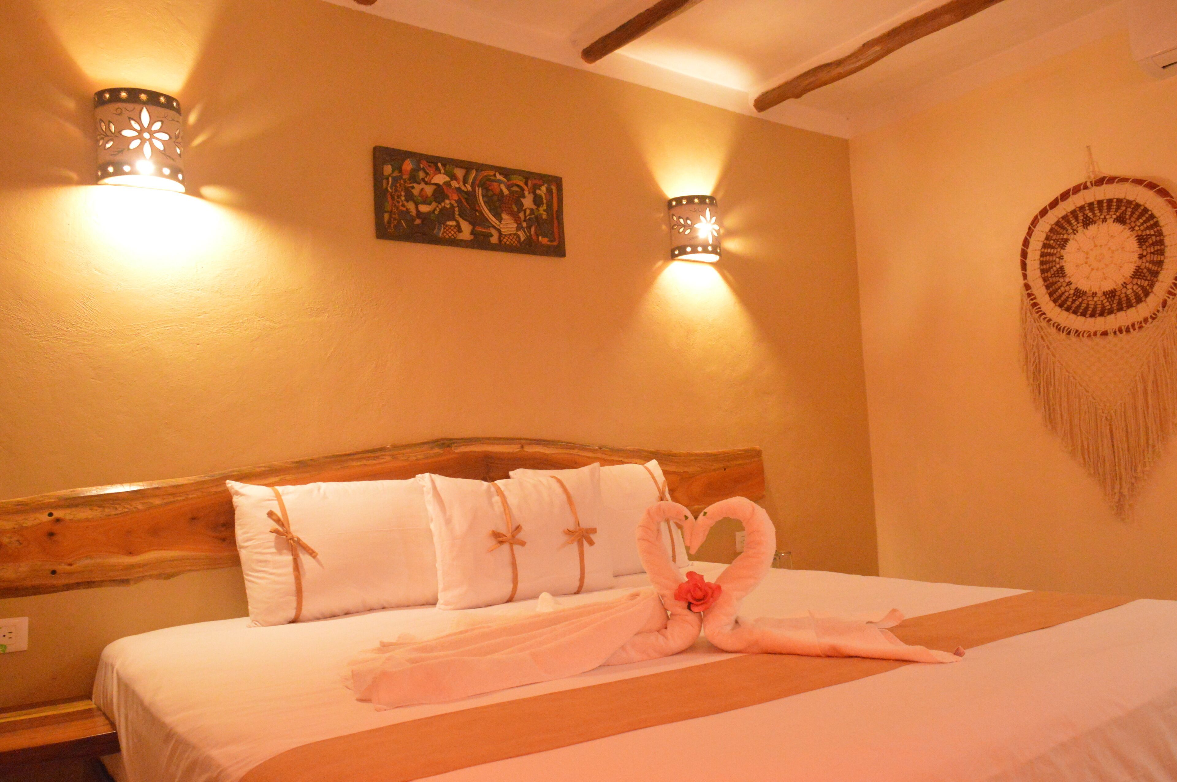 Una habitación de hotel con una cama, dos lámparas de pared, una obra de arte en la pared y un adorno colgante.