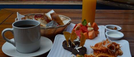 Une table mise pour le petit-déjeuner avec une tasse de café, un verre de jus d’orange et une assiette contenant des œufs brouillés, des haricots et des légumes.