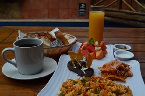 Une table mise pour le petit-déjeuner avec une tasse de café, un verre de jus d’orange et une assiette contenant des œufs brouillés, des haricots et des légumes.