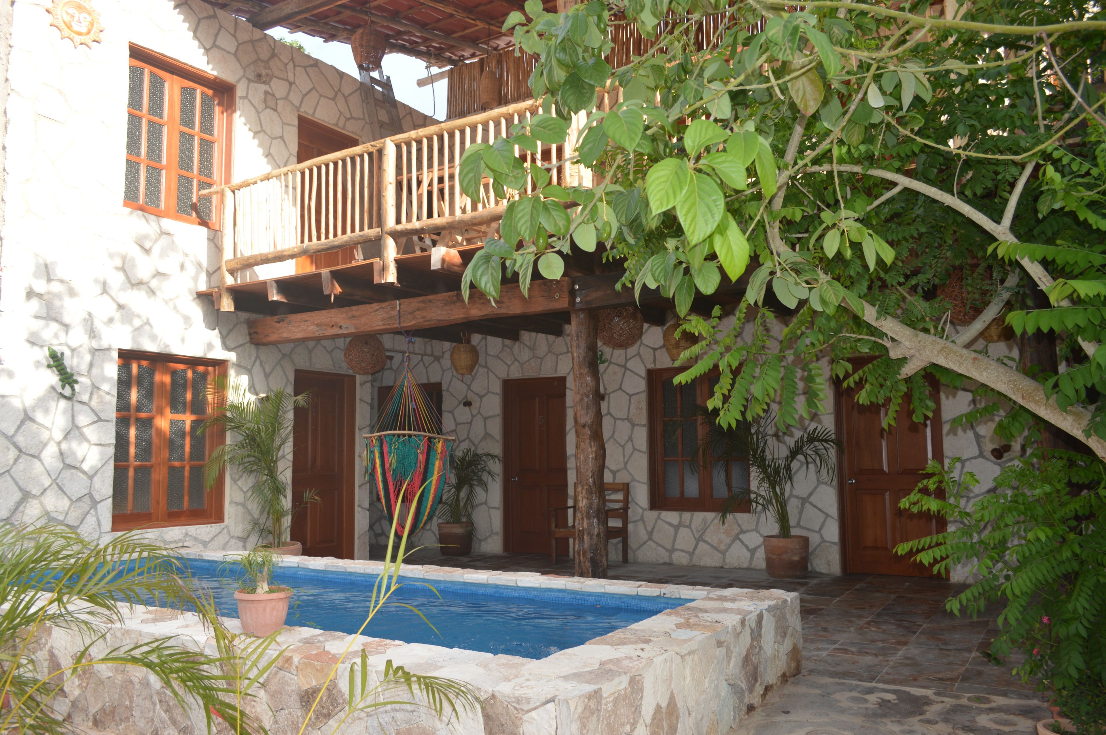 Un edificio de piedra con balcón de madera, piscina y plantas en macetas.