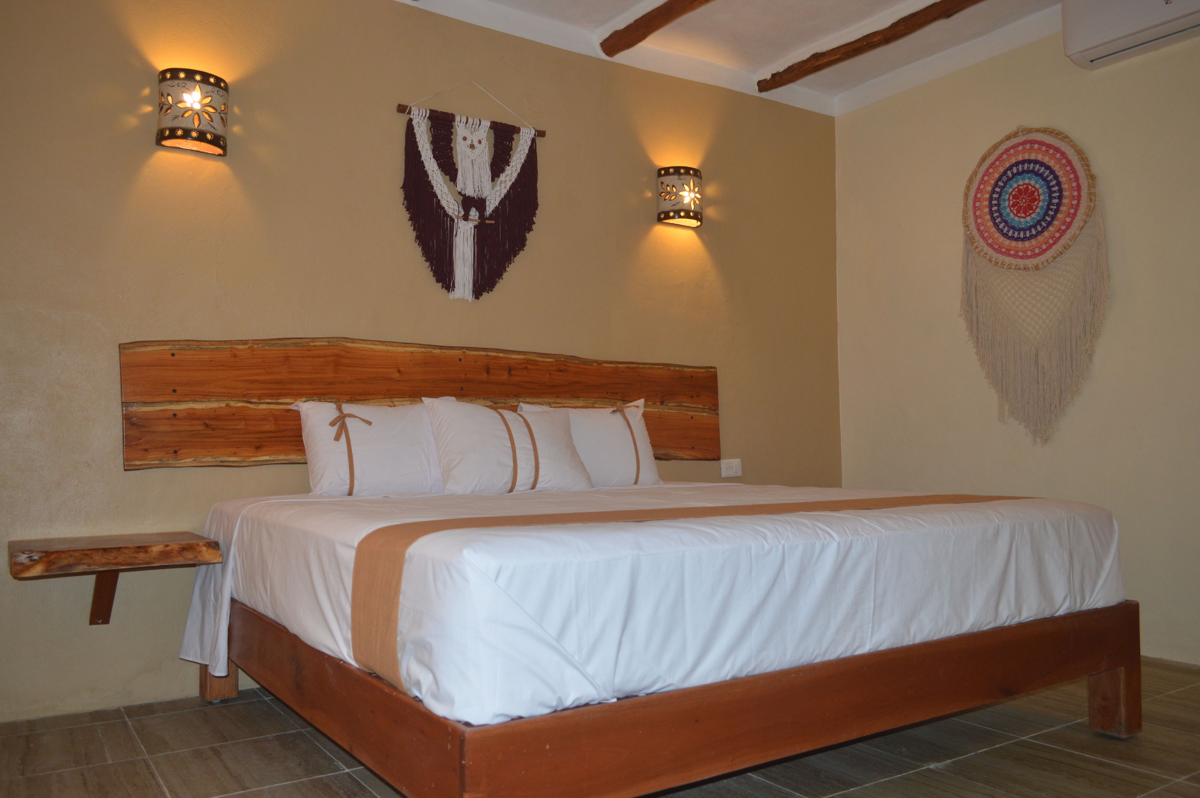 Una cama con cabecera de madera, dos lámparas de pared y un adorno colgante en la pared.