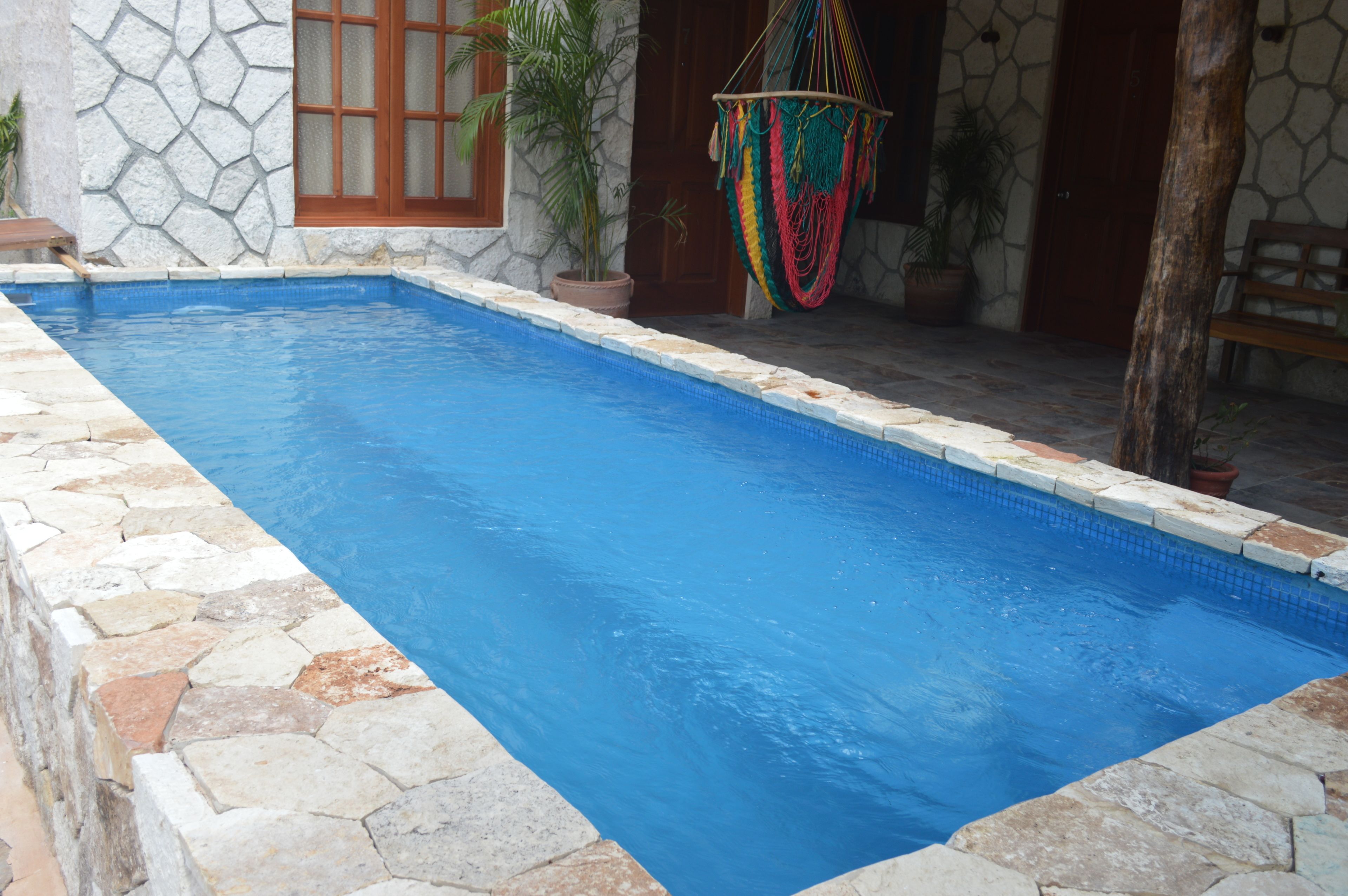 Piscina rectangular con baldosas de piedra, rodeada por un muro de piedra y una puerta de madera.