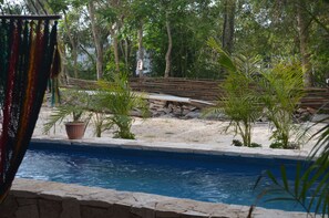 Une piscine bordée de pierres, entourée de palmiers et délimitée par une clôture en bois.