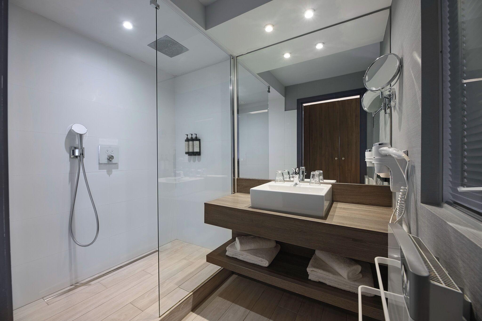 Une salle de bain moderne dotée d’une douche à parois de verre, d’un grand miroir et d’un lavabo intégré.
