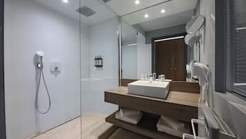 Une salle de bain moderne dotée d’une douche à parois de verre, d’un grand miroir et d’un lavabo intégré.