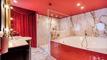 A bathroom with a marble vanity, a large bathtub, and a red curtain.