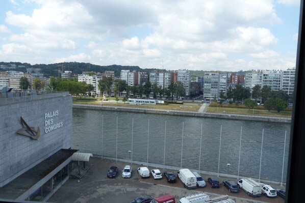 A view of a parking area with vehicles, a river, and buildings in the background. - Van der Valk Hotel Liège Congrès (Liege)
