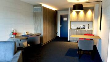 A compact hotel room with a kitchenette, a dining area, and a seating area.