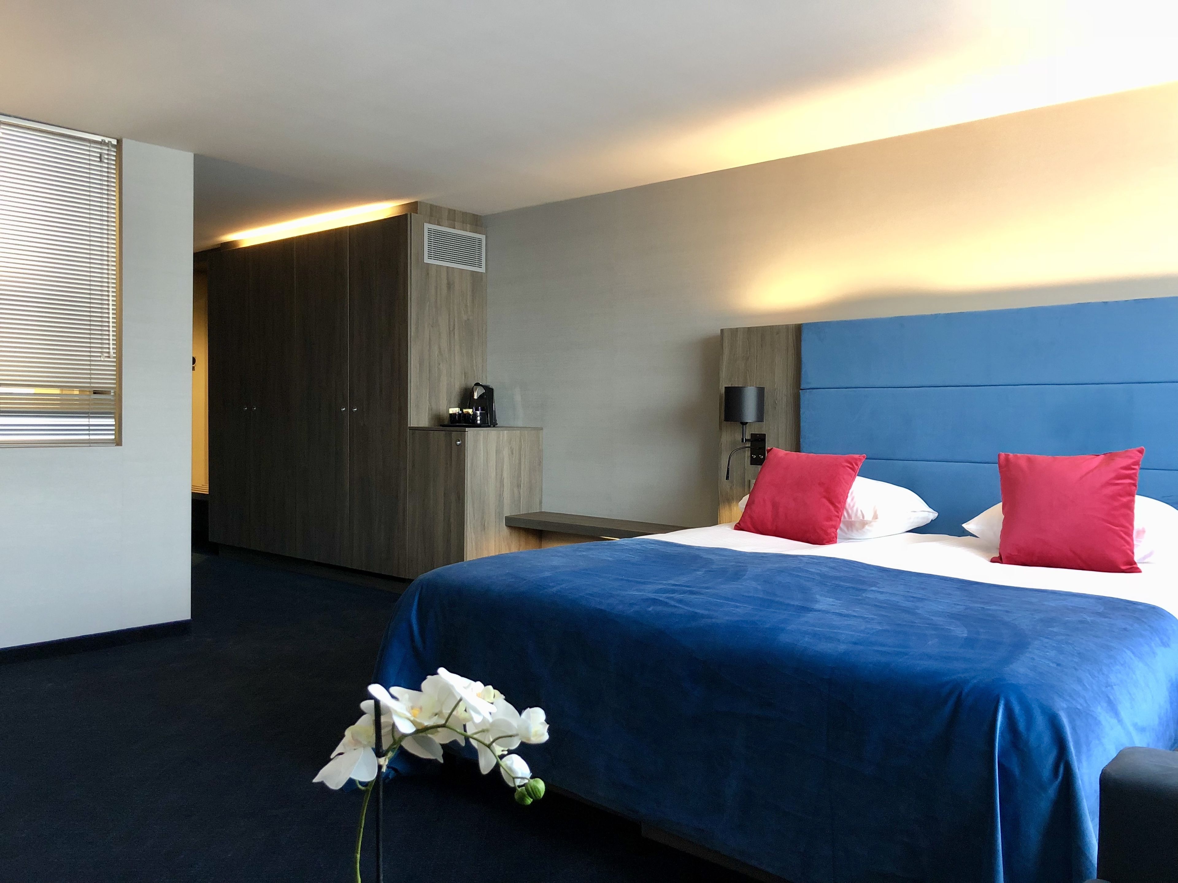 A hotel room with a large bed, a wardrobe, a desk, and a nightstand.