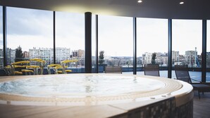 Un jacuzzi con vistas a la ciudad, ventanas amplias y sillas amarillas.