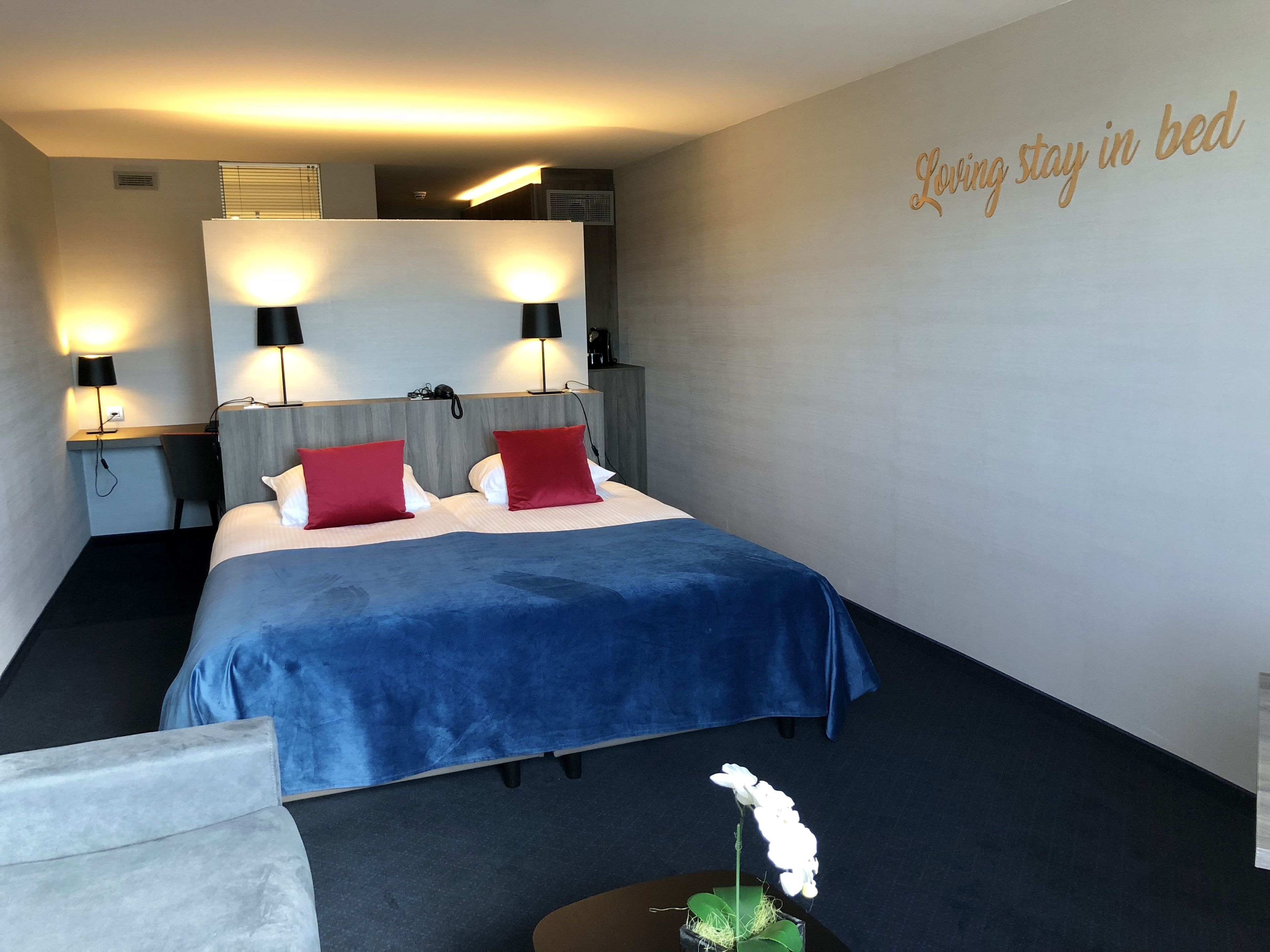 A hotel room with a bed, two bedside lamps, a desk, and a chair.