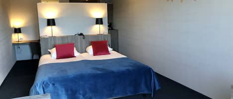 A hotel room with a bed, two bedside lamps, a desk, and a chair.