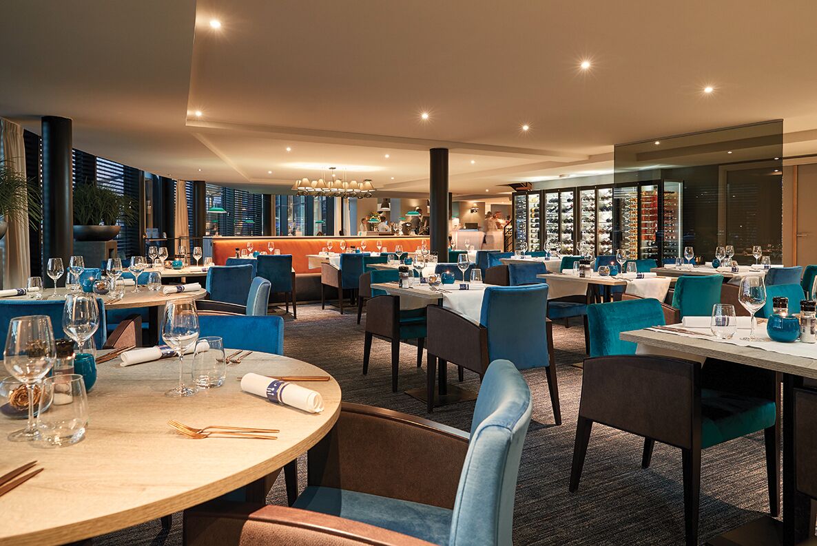 A restaurant with round tables, blue chairs, and a bar area.