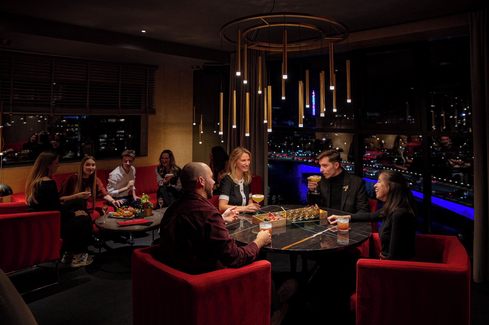 A group of people dining at a table in a dimly lit restaurant with a city view.