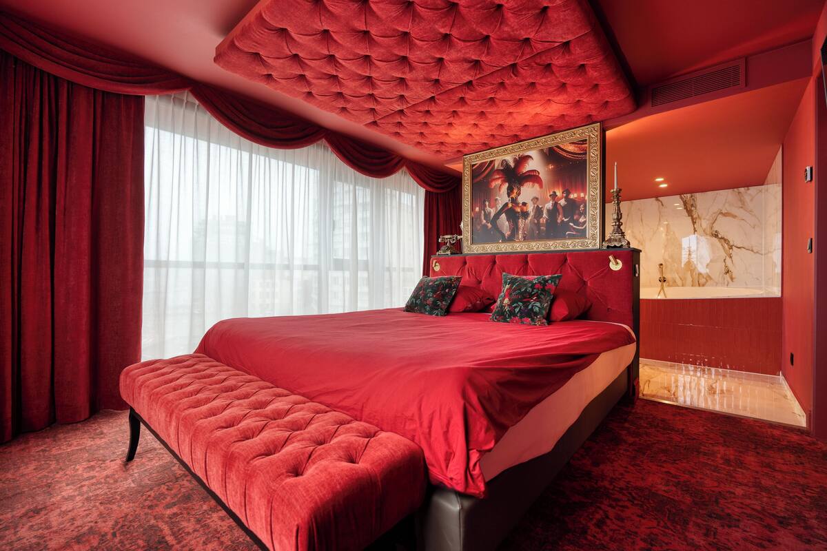 Une chambre à coucher aux couleurs rouge, avec un grand lit, une tête de lit capitonnée et un mur en marbre.