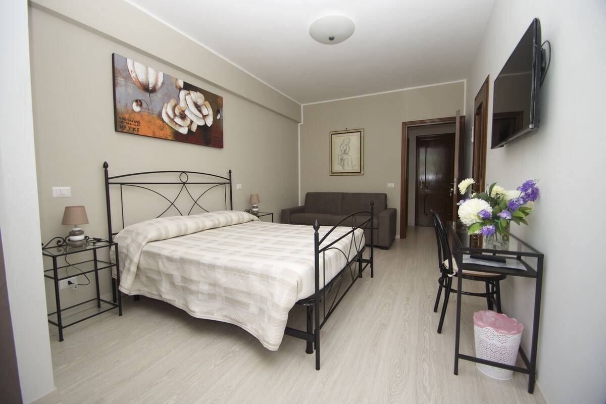 A bedroom with a bed, bedside table, lamp, and a TV mounted on the wall.