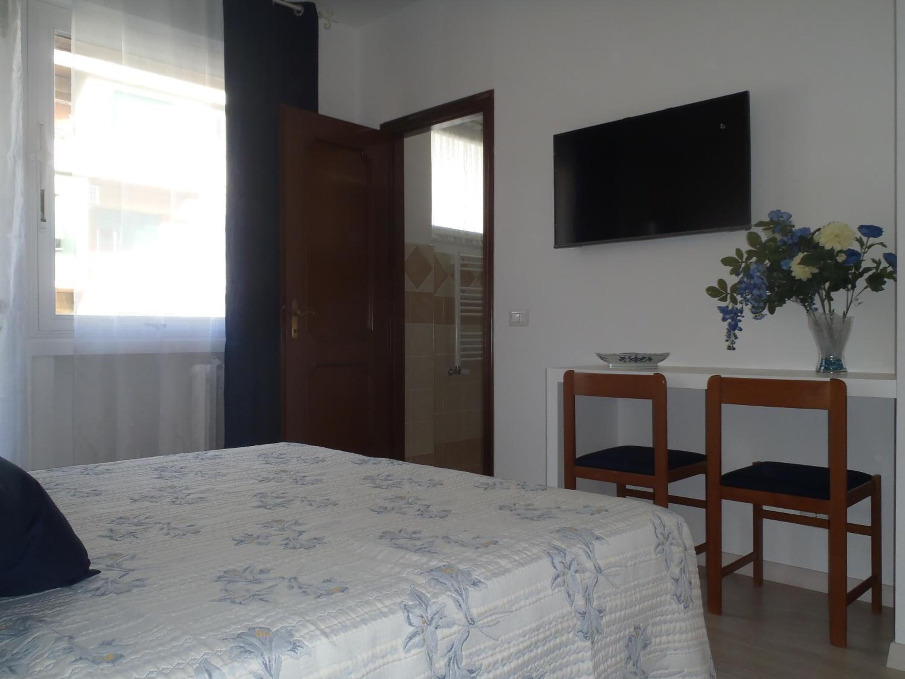 A bedroom with a bed, a TV mounted on the wall, and two chairs.