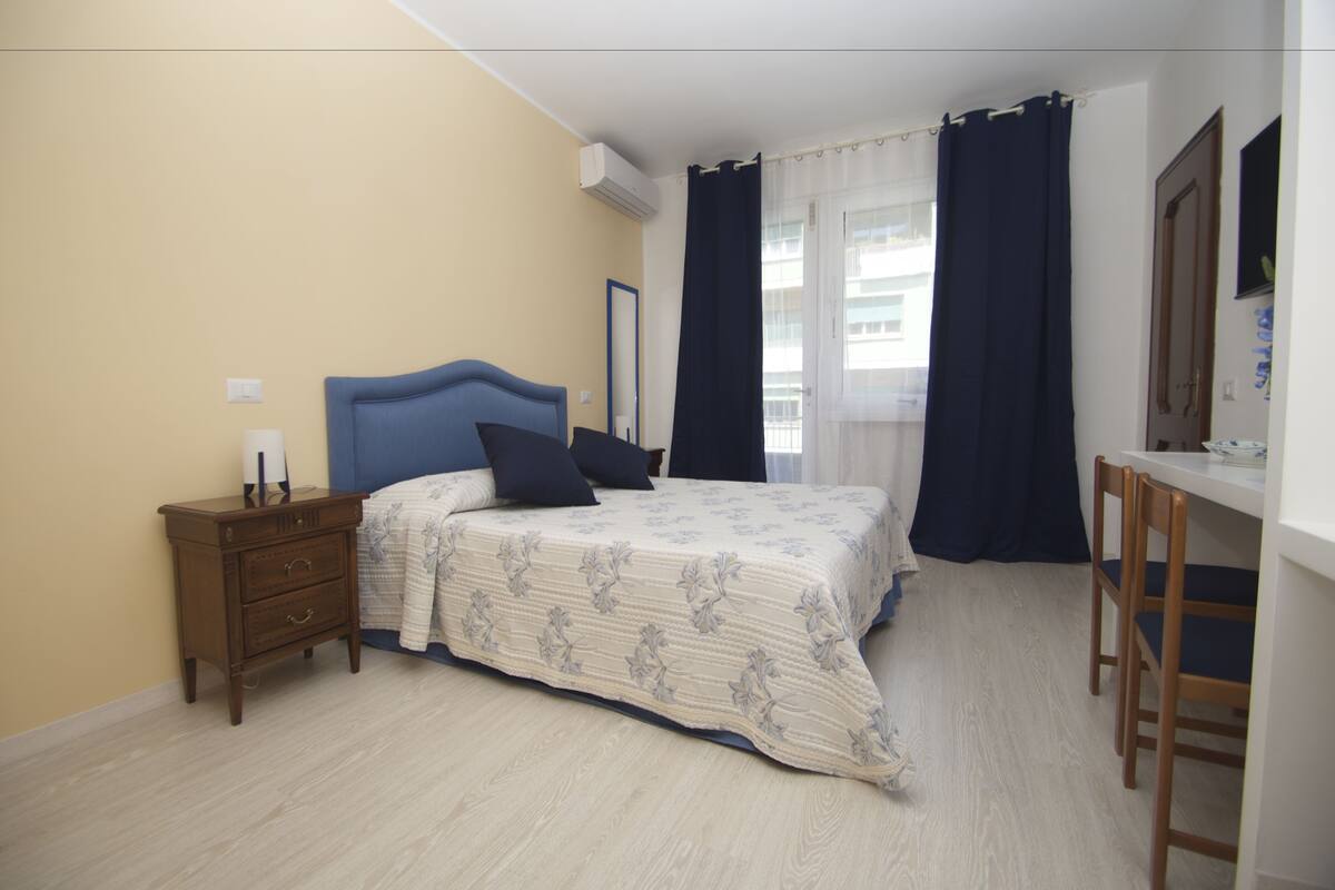 A bedroom with a bed, a nightstand, a desk, and a chair.