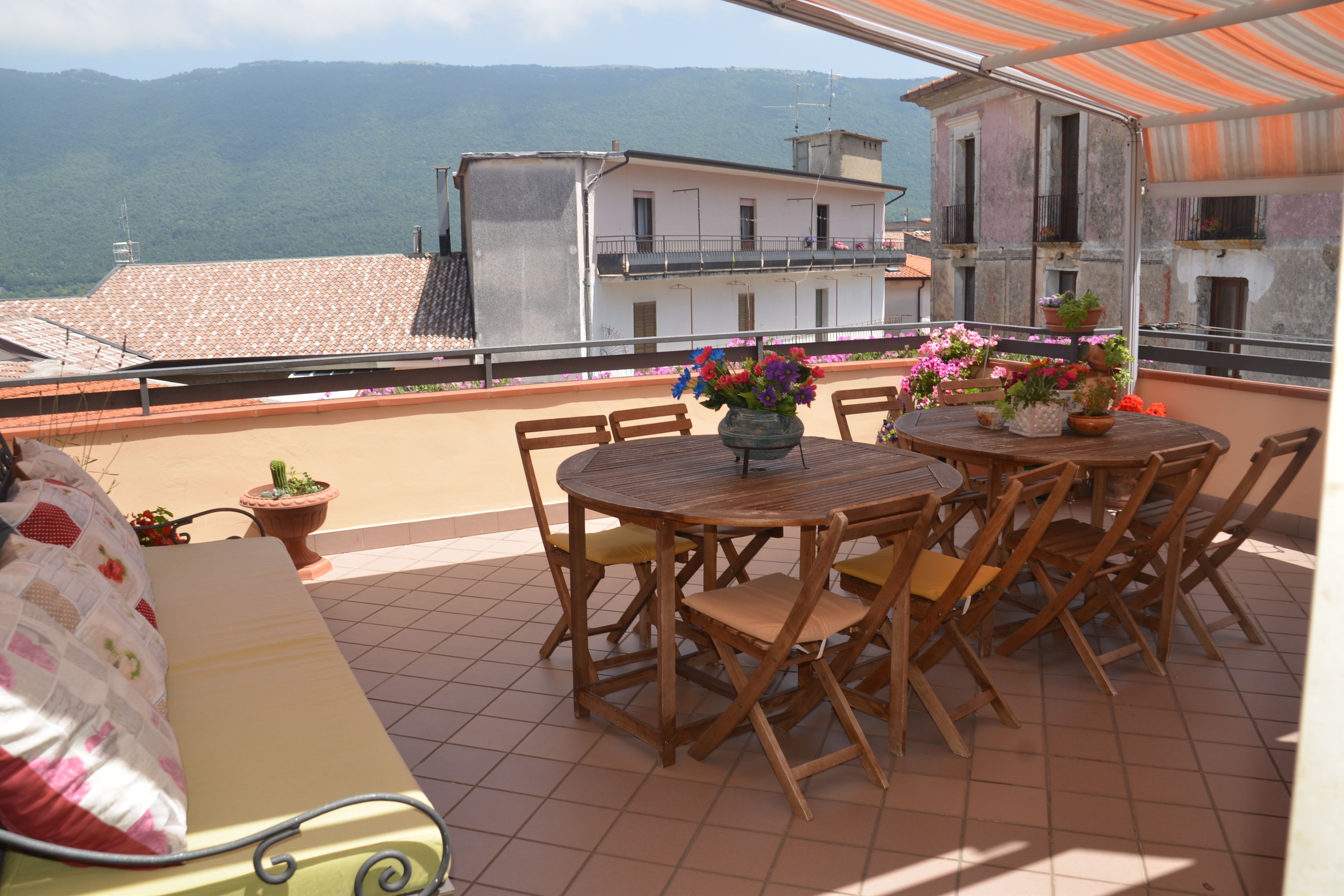 Una terrazza con un tavolo e sedie di legno rotonde, una panca imbottita e piante in vaso.