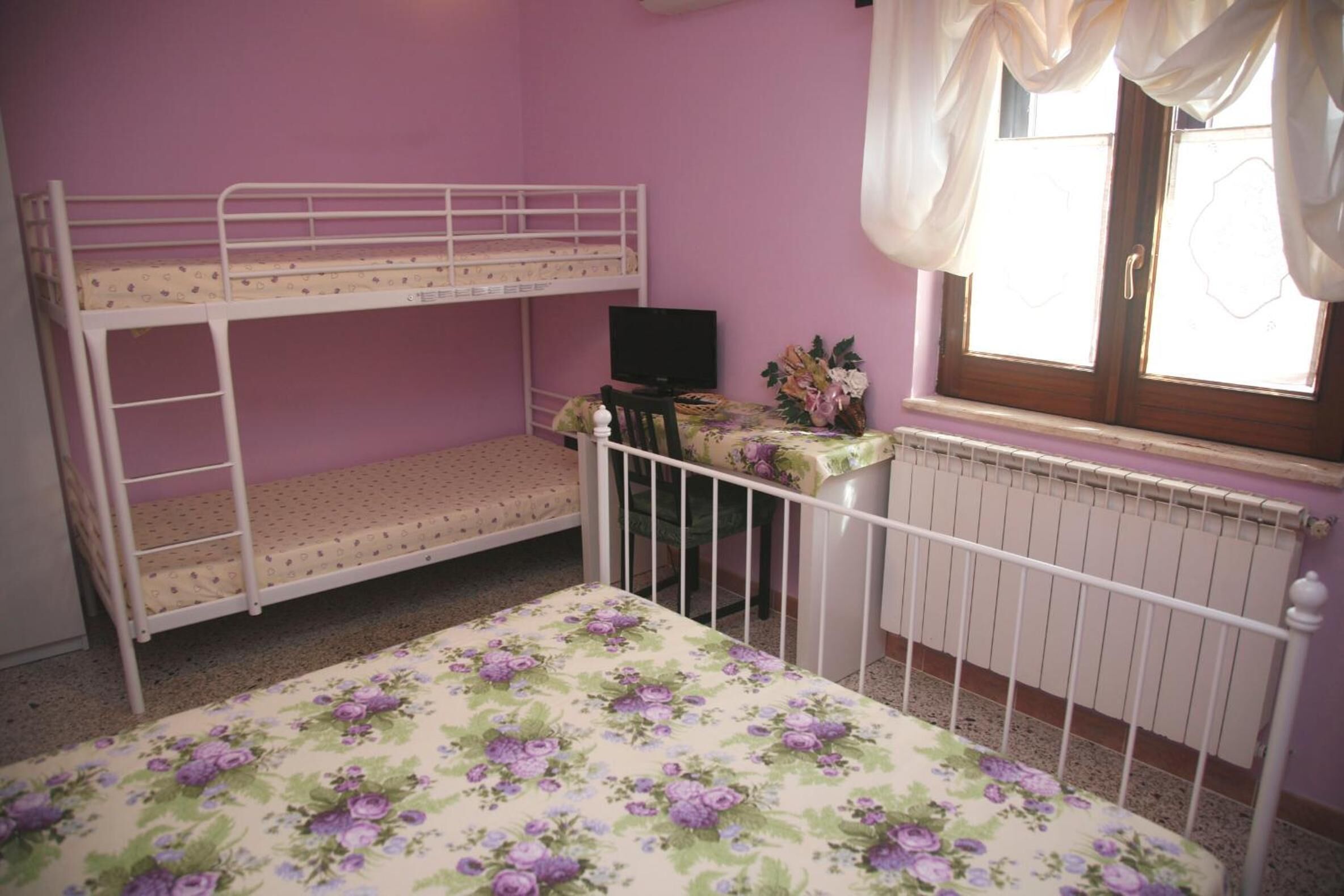 Ein Zimmer mit Etagenbetten, einem Schreibtisch, einem Stuhl, einem Heizkörper und einem fenster mit Vorhängen.