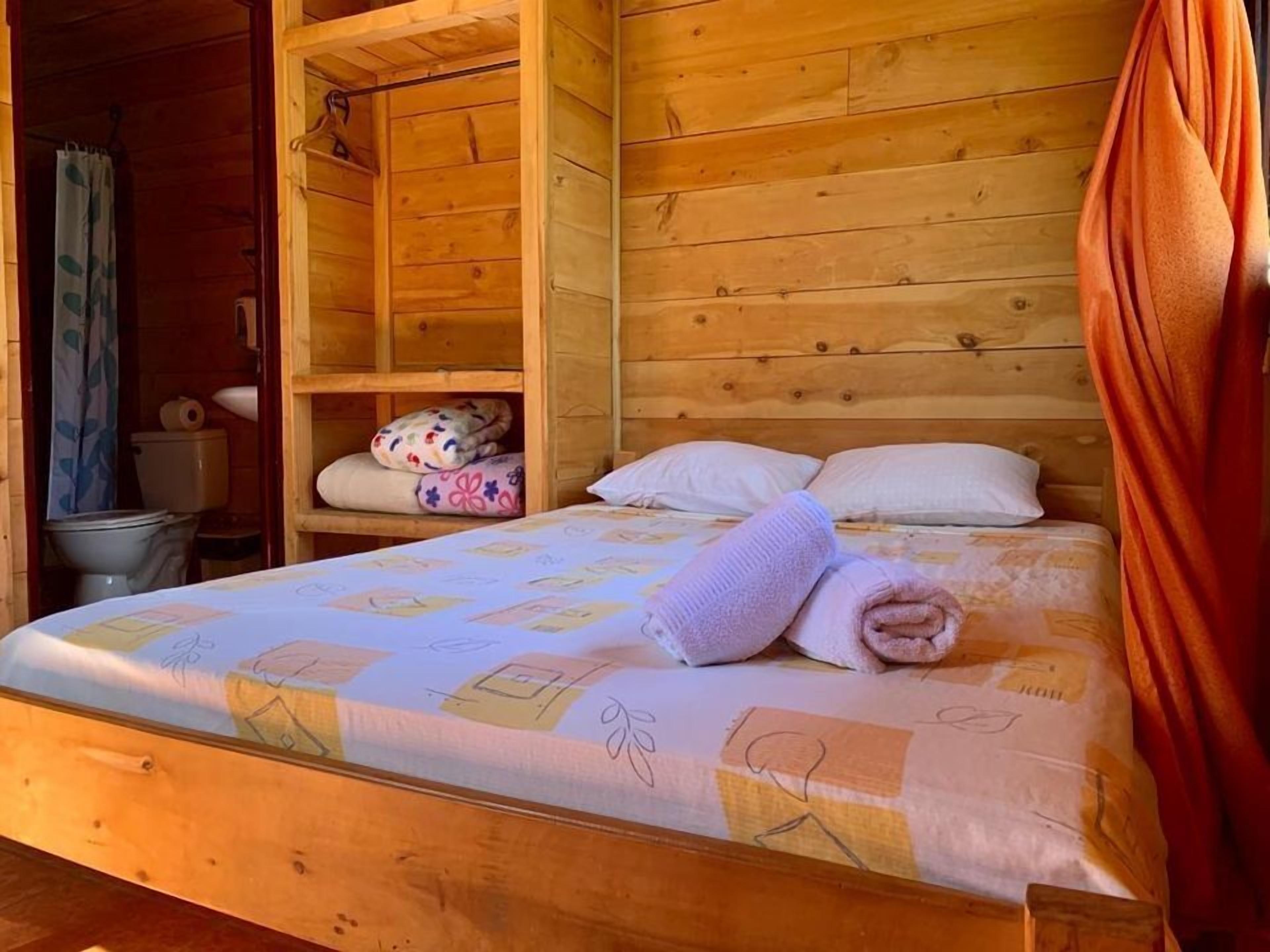 Quarto de cabana de madeira com cama, banheiro pequeno e armário de madeira.