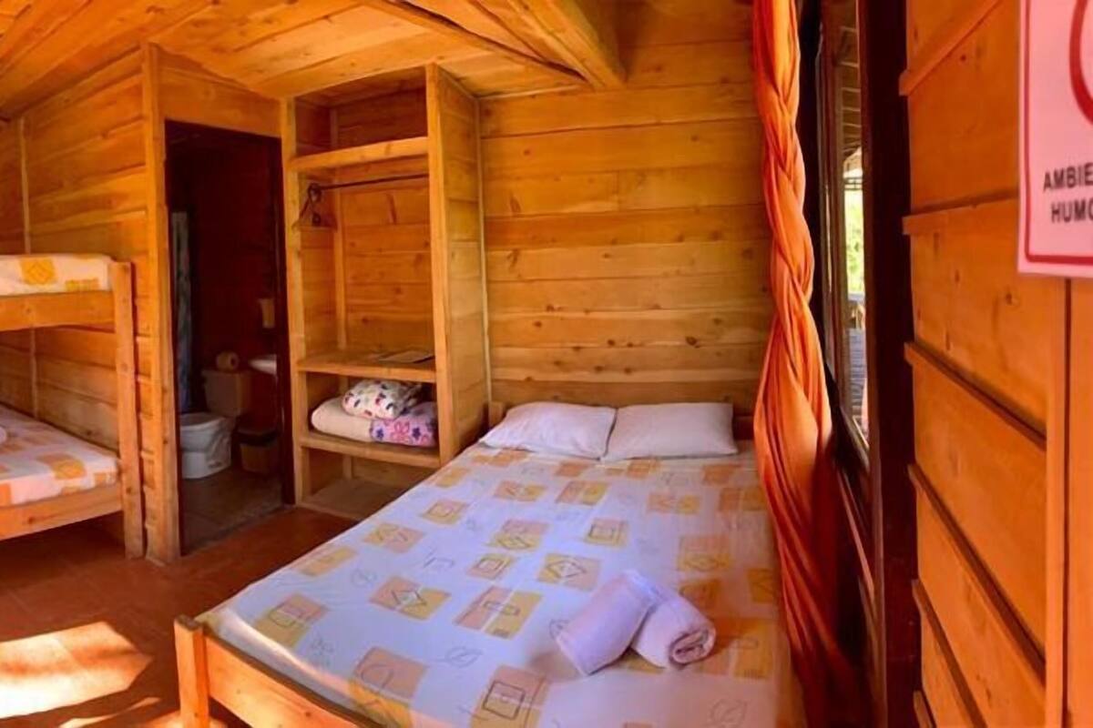 Una cabaña de madera con literas, un baño pequeño y una puerta visible.