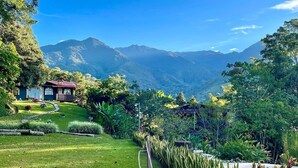 Uma casa com telhado vermelho, rodeada por vegetação exuberante e um cenário montanhoso.