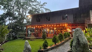 Um edifício com área externa coberta, caminho pavimentado e um jardim bem cuidado com pedras e arbustos.