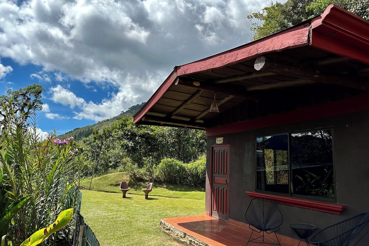 Un pequeño edificio con techo rojo y ventana, rodeado de césped y árboles.