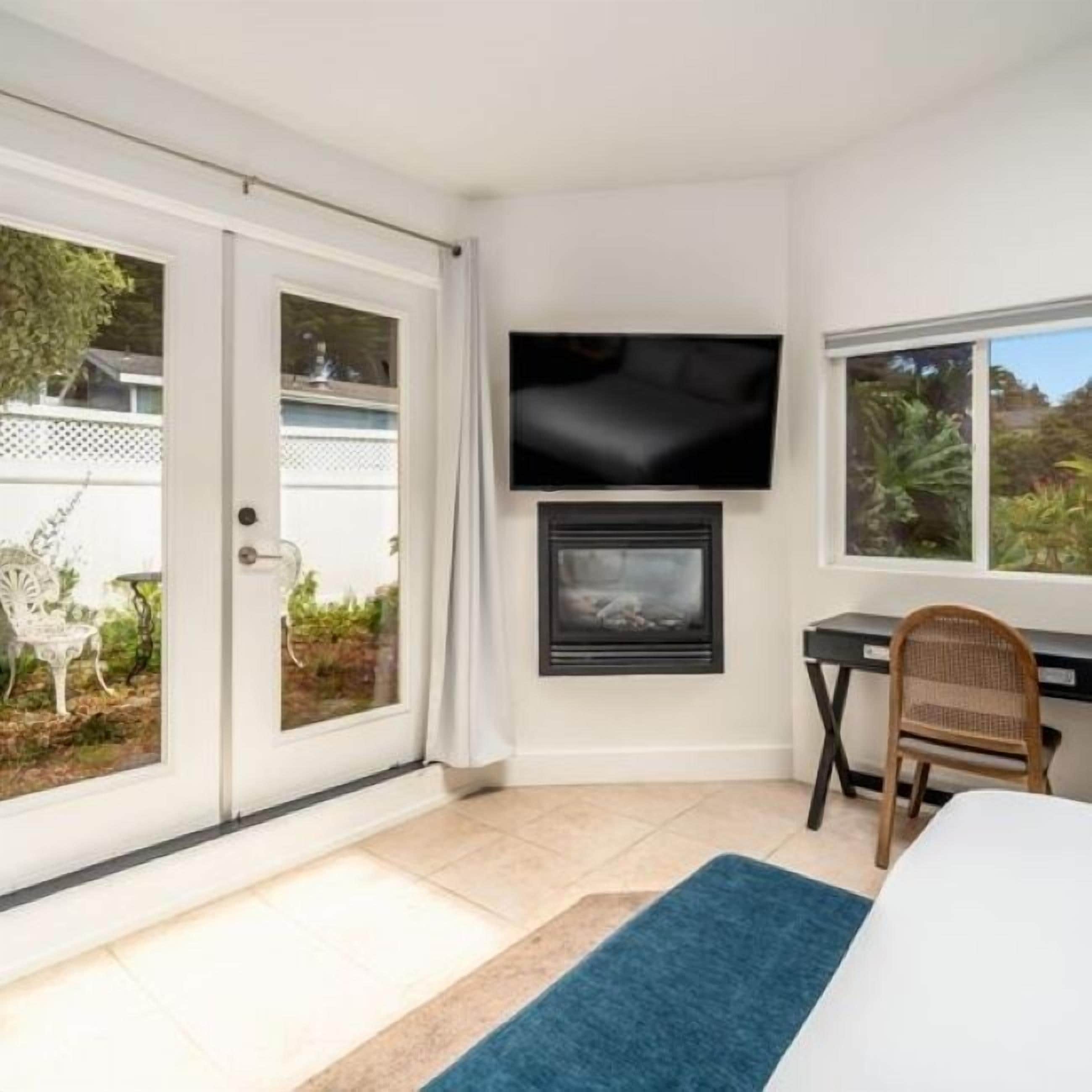 A room with a TV mounted above a fireplace, a desk with a chair, and a view through a glass door.