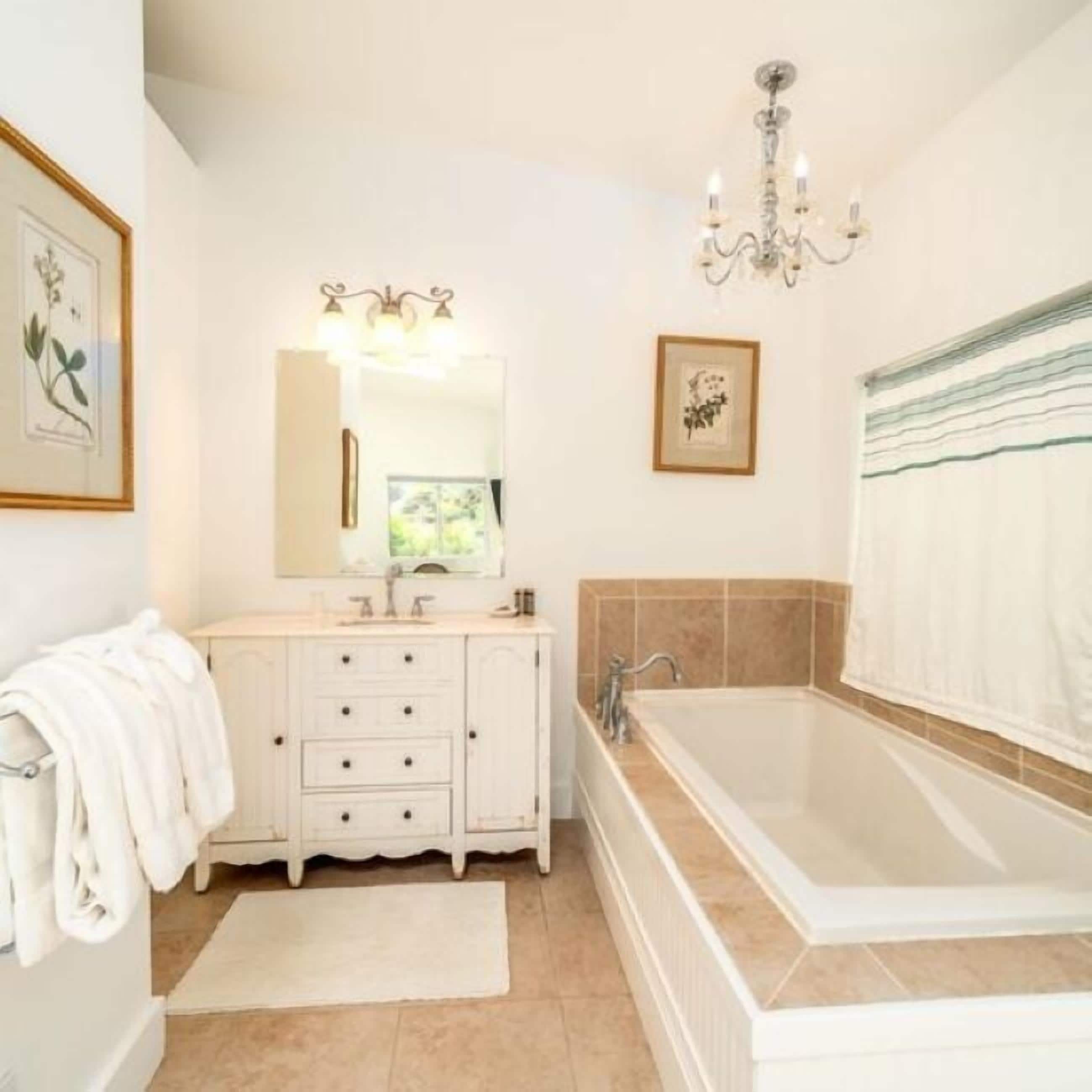 A bathroom with a large bathtub, a vanity with a mirror, and a chandelier.