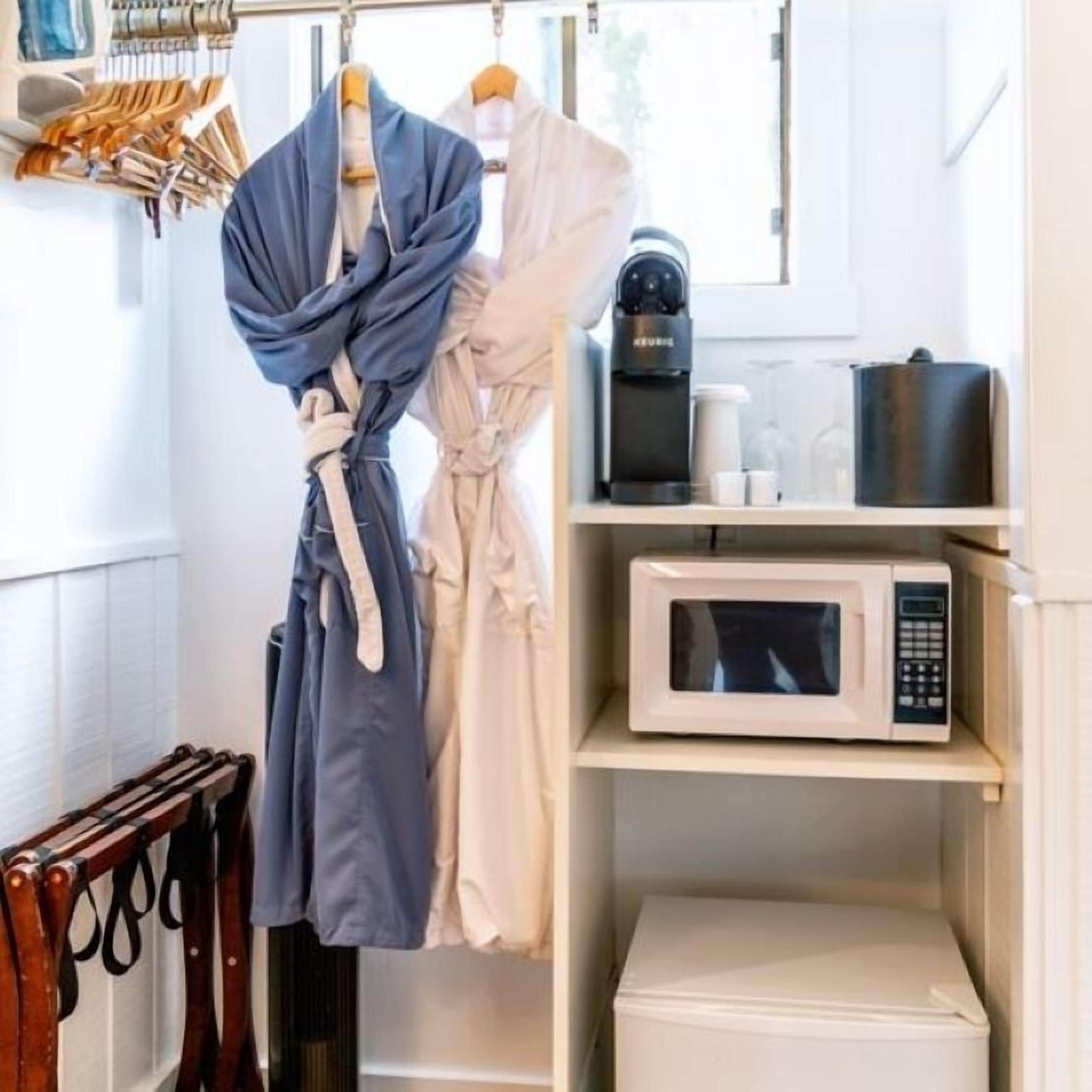 A hotel room with a robe rack, a coffee maker, a microwave, and a small cabinet.