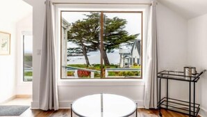A modern room with a large window, a round table, and a black metal shelf. - Agate Cove Inn (Mendocino)