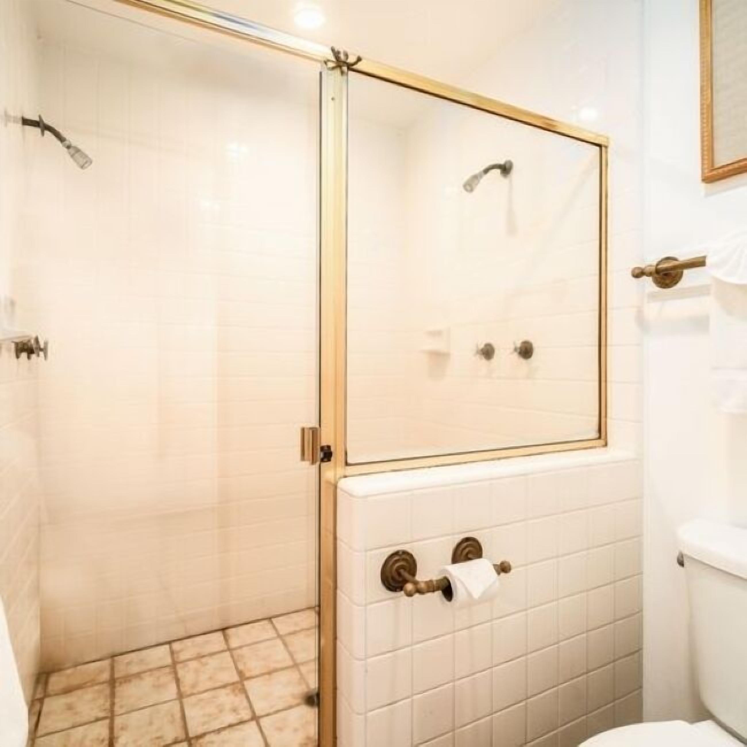 Een badkamer met een douche met glazen wand, witte betegelde wanden en een toilet met een papieren handdoekhouder.