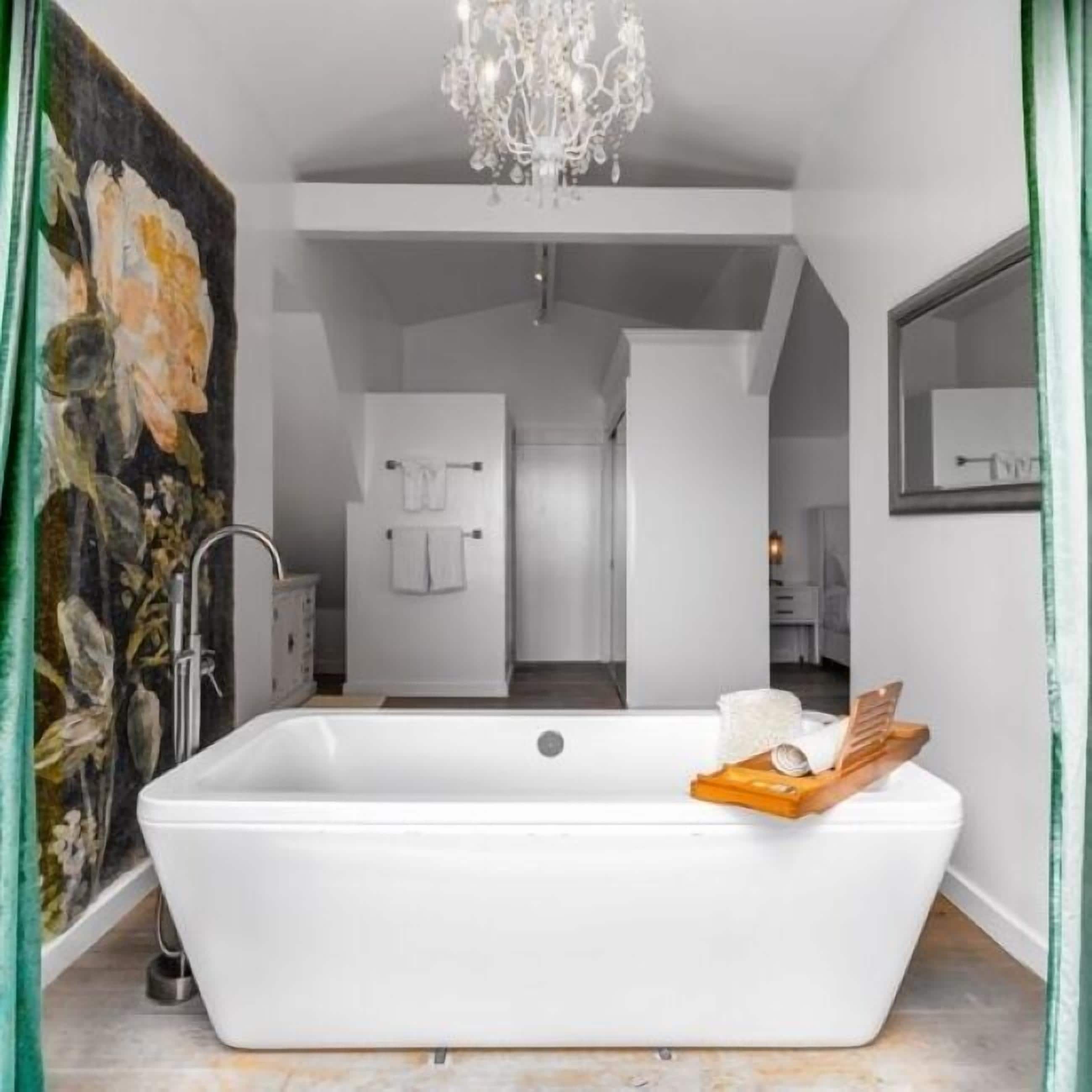 Een moderne badkamer met een vrijstaand bad, een kroonluchter en een grote spiegel.
