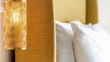 Una cama moderna con cabecera dorada, una mesita de noche con lámpara dorada y ropa de cama blanca.