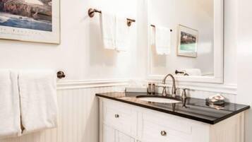 A bathroom with a white vanity, a sink, and a mirror. There is a framed picture on the wall above the mirror.