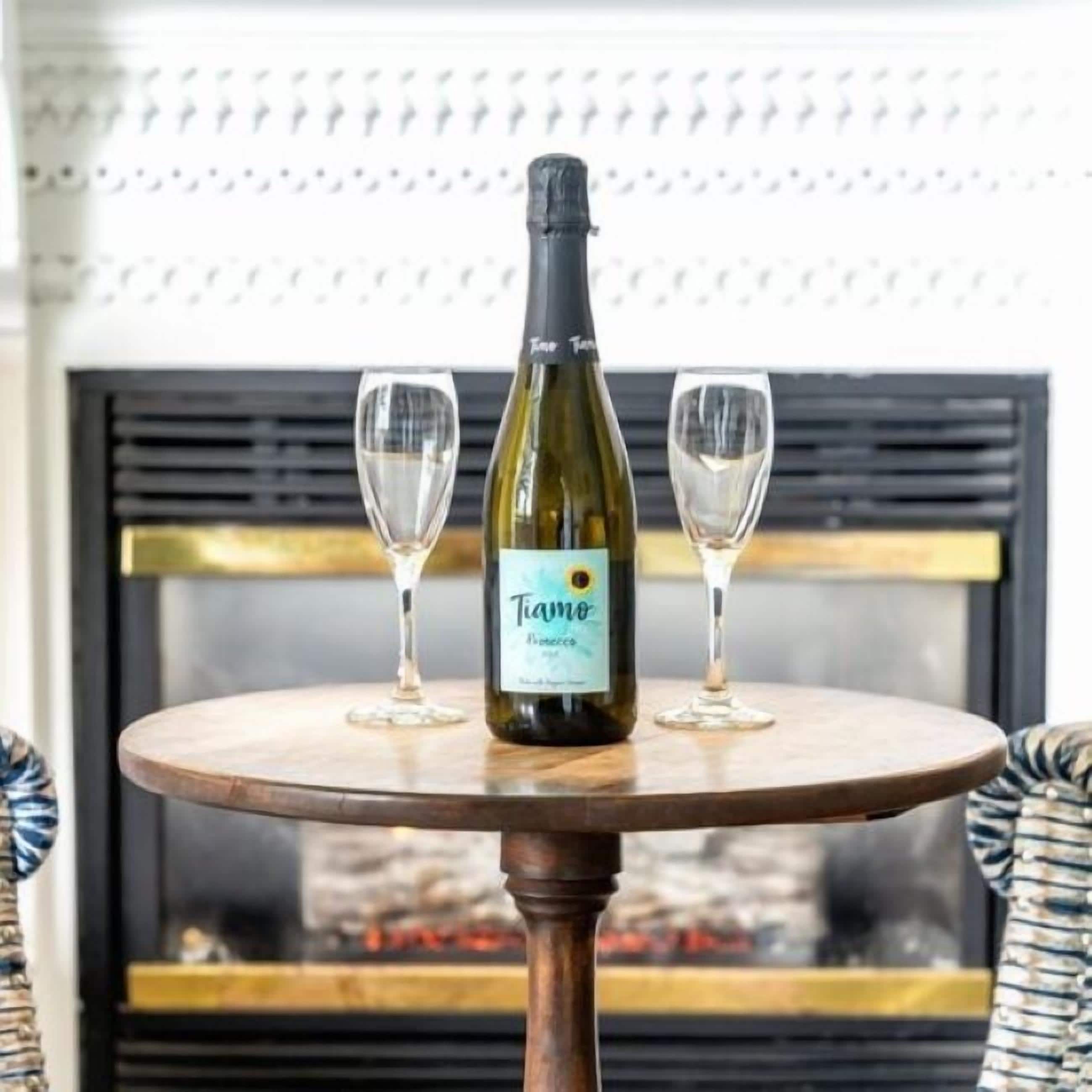 A bottle of wine and two glasses on a round wooden table.