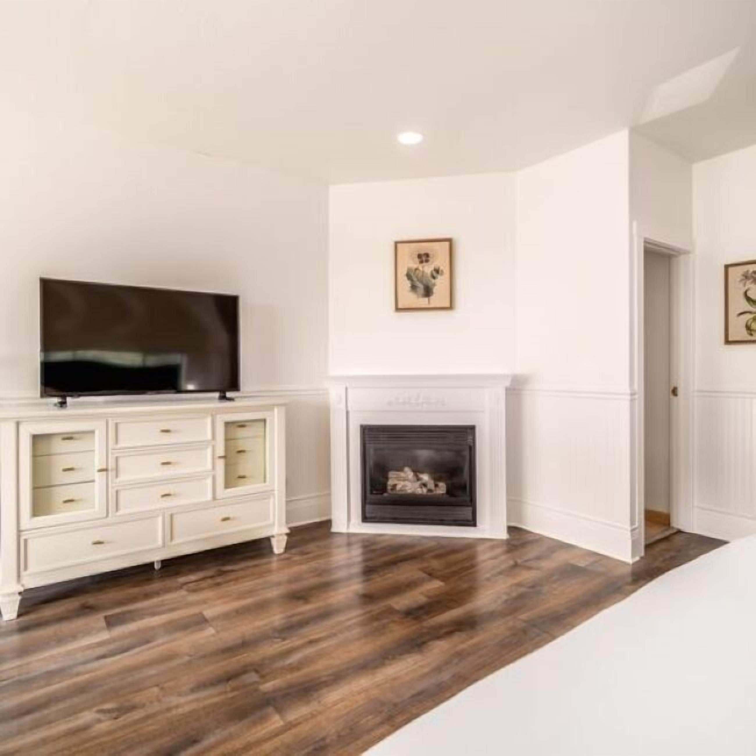 A bedroom with a TV on a white dresser, a fireplace, and two framed pictures on the wall.