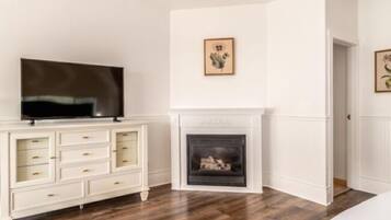 A bedroom with a TV on a white dresser, a fireplace, and two framed pictures on the wall.