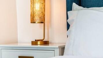 A bed with white bedding, a bedside table with a gold lamp, and a blue curtain in the background.