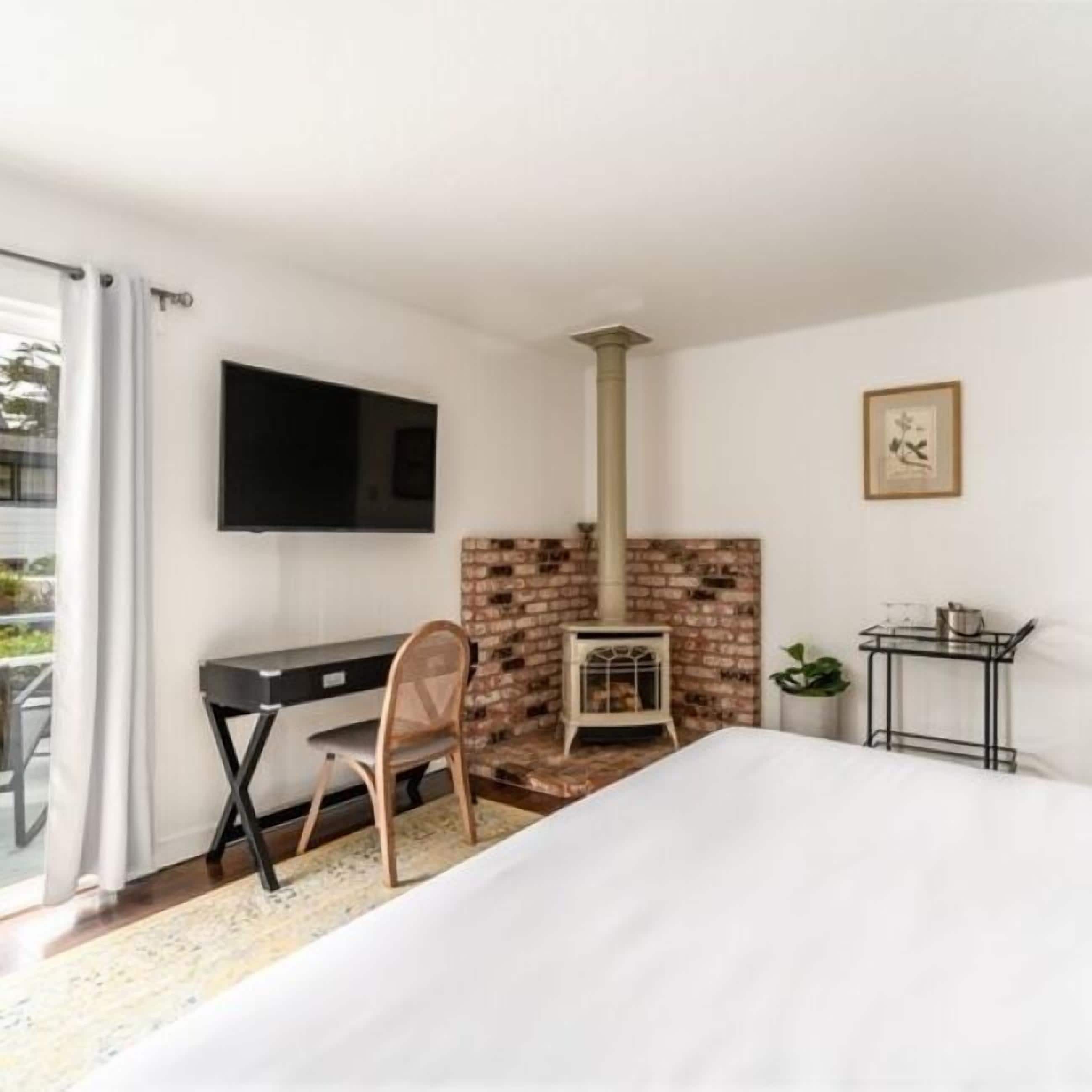 Une chambre à coucher comprenant un lit, un bureau, une chaise, une télévision, une cheminée et une petite table avec une plante.