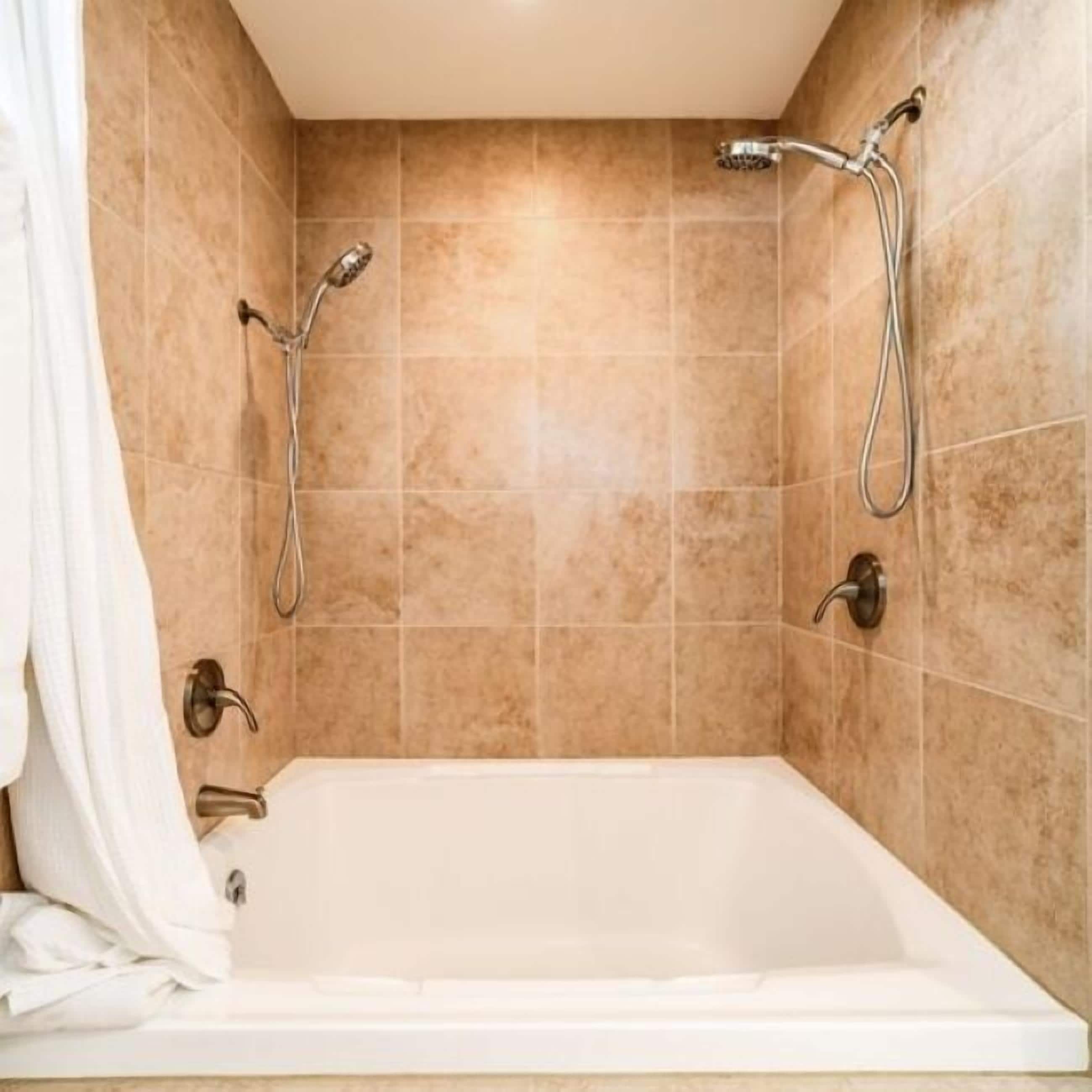 Een moderne badkamer met een vrijstaand bad, twee douches en beige wandtegels.
