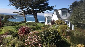 A coastal house with a view of the ocean, surrounded by lush greenery and flowering plants. - Agate Cove Inn (Mendocino)