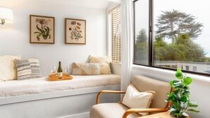 A cozy room with a sofa, a wooden side table, and a window with a view of trees. - Agate Cove Inn (Mendocino)